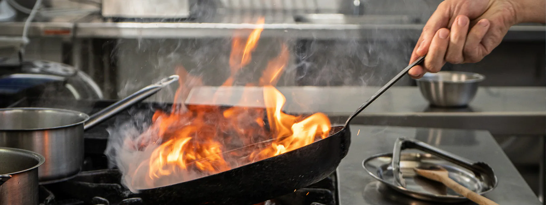 Una sartén en llamas sobre la hornalla de una cocina profesional.